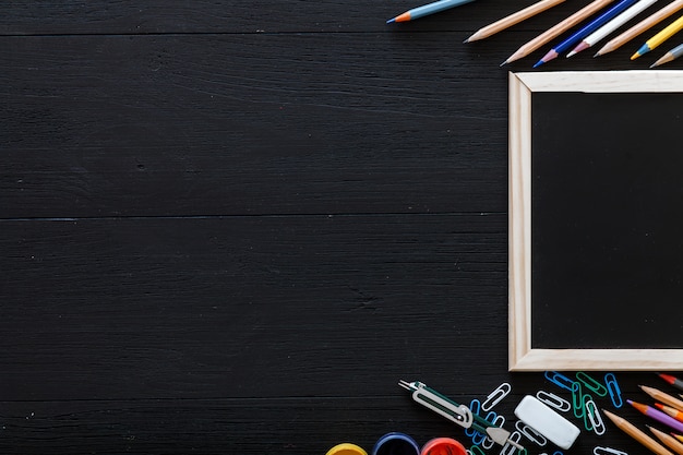 Fondo de regreso a la escuela con artículos de papelería para la educación primaria moderna, lápices de colores, pinturas y marco en pupitre de madera negra oscura, espacio de copia gratuita para texto, vista superior desde arriba