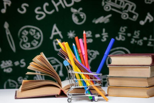 Fondo de regreso a la escuela con libros, lápices y globo en mesa blanca sobre un fondo verde pizarra.