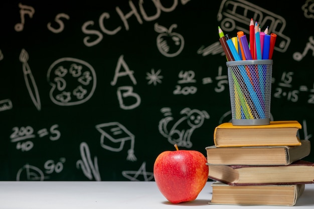 Fondo de regreso a la escuela con libros, lápices y manzana en mesa blanca.