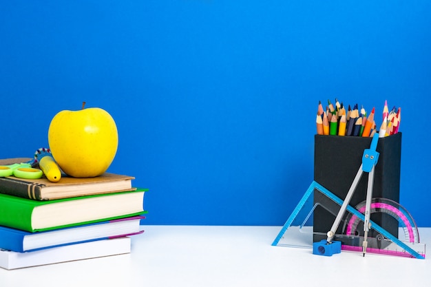 Fondo de regreso a la escuela con libros, lápices y manzana en mesa blanca