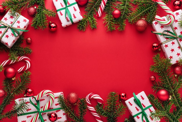 Fondo rojo de Navidad y año nuevo. Marco decorativo de ramas de abeto, regalos, bolas de Navidad y bastón de caramelo. Copie el espacio para la fluencia navideña