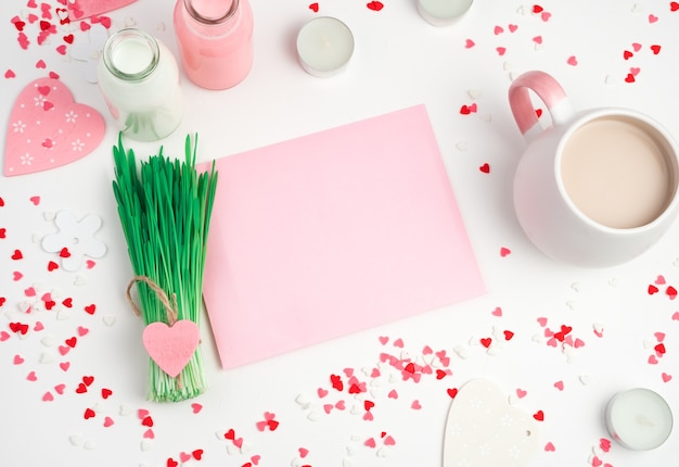 Fondo romántico con corazones, taza de café, sobre rosa y un montón de hierba sobre un fondo claro. Vista superior con espacio para copiar. En tonos rosados. Concepto del 14 de febrero, día de la mujer.