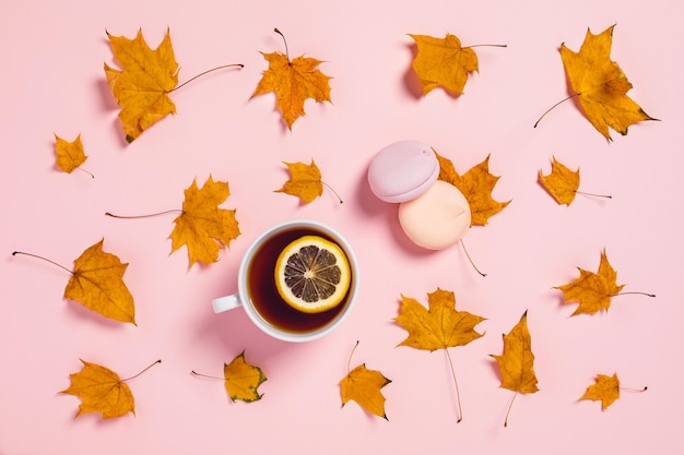 Fondo rosa con taza de té y limón rodeado de hojas de arce naranja y malvaviscos