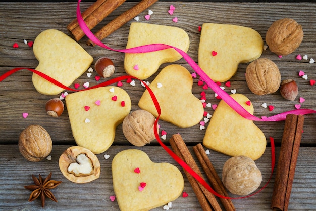 Fondo de San Valentín con galletas en forma de corazón, corazones de colores, cintas y canela.