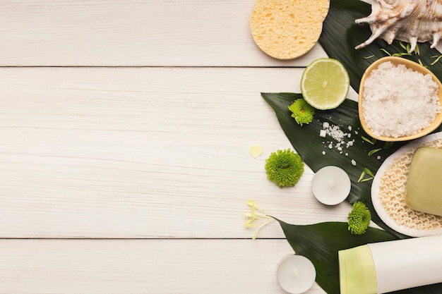 Fondo de spa. Sal marina natural y jabón hecho a mano con loción sobre hojas verdes en la mesa blanca. Salón o cuidado del cuerpo y la piel en el hogar, espacio de copia, vista superior