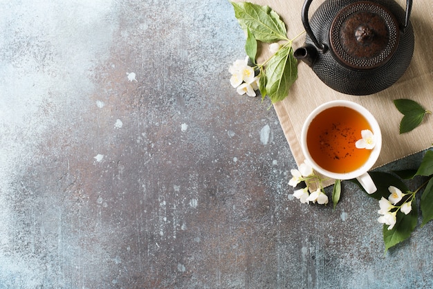 Fondo de té jazmín con tetera, hojas y flores de textura oscura, vista superior, espacio de copia