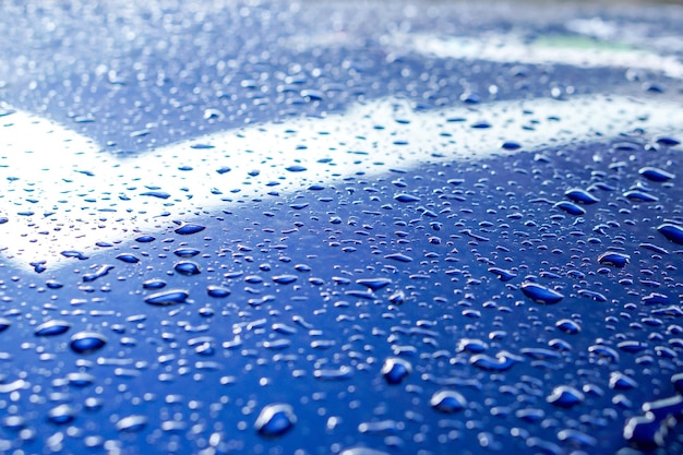 Fondo y textura de las gotas de lluvia y la iluminación de reflexión sobre el capó del motor del coche azul