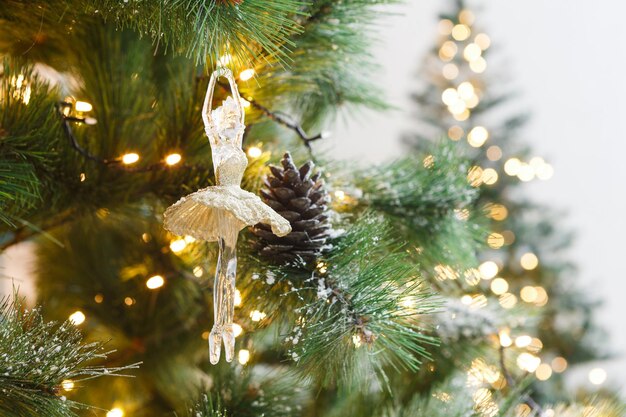 Fondo de vacaciones de árbol de Navidad. Magia y belleza navideñas. Ramas de pino esponjosas con piñas con nieve y decoradas con una elegante bailarina de juguete y guirnaldas, primer plano, espacio de copia, enfoque selectivo