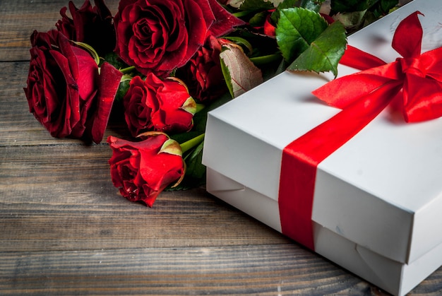 Fondo de vacaciones, día de San Valentín. Ramo de rosas rojas, corbata con una cinta roja, con caja de regalo envuelta. En la mesa de madera, copie el espacio