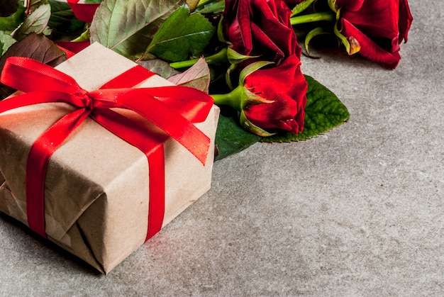 Fondo de vacaciones, día de San Valentín. Ramo de rosas rojas, corbata con una cinta roja, con caja de regalo envuelta y vela roja