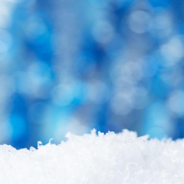 Foto fondo de vacaciones de navidad cubierto de nieve con nieve y brillante telón de fondo borroso. blanca nieve con brillo azul bokeh. decoración para las vacaciones de año nuevo.