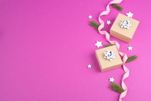 Fondo de vacaciones de Navidad con pequeñas cajas de regalo, estrellas y ramas de abeto, fondo rosa de moda