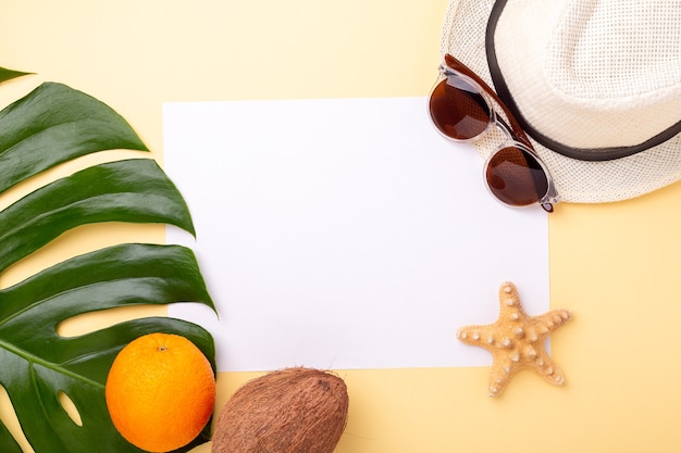 Fondo de vacaciones de verano. Papel en blanco, hoja de monstera y frutas exóticas sobre fondo amarillo