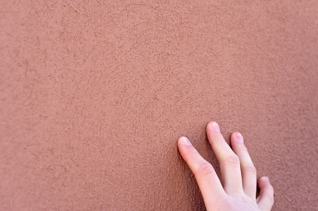 Fondo vacío Pared naranja textura porosa Los dedos del joven tocan la superficie de la pared pintada del edificio Los dedos se cierran