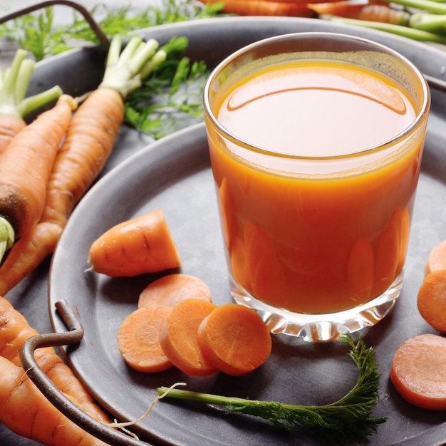 Fondo vegetariano de bandeja antigua con zanahorias orgánicas frescas y jugo en la mesa de madera de la cocina