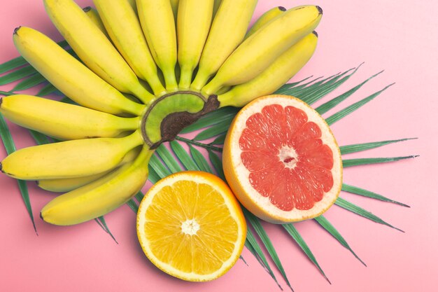 Fondo de verano de frutas tropicales. Plátanos, naranjas y pomelos sobre un fondo de color rosa.