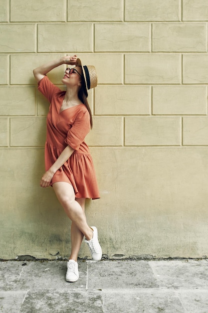 Fondo de verano. Hermosa joven con un sombrero de paja y un vestido naranja sobre fondo de color. Vistas a la ciudad.