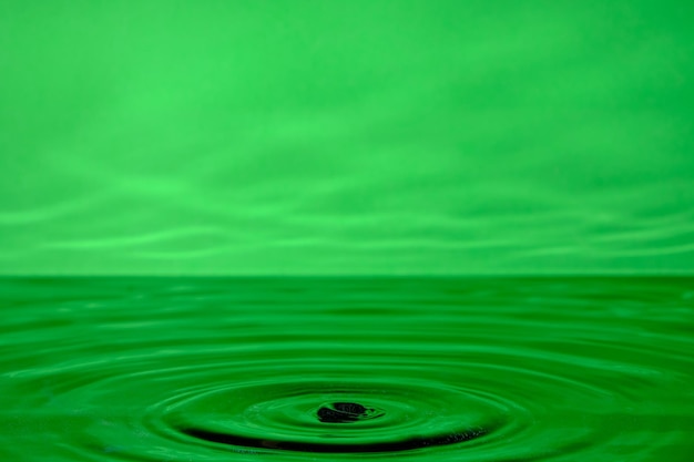 Fondo verde brillante con círculos divergentes de una gota caída en el agua superficial.