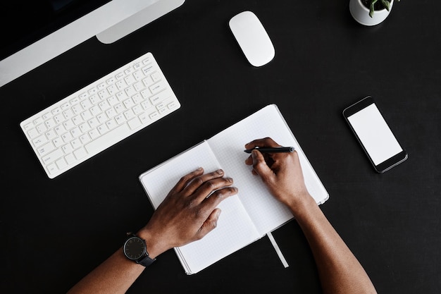 Fondo de vista superior mínima de manos masculinas escribiendo en planificador en el espacio de copia de escritorio negro