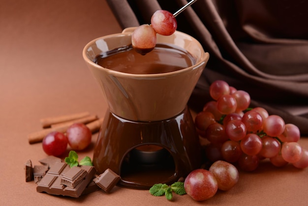 Fondue de chocolate con frutas sobre fondo marrón