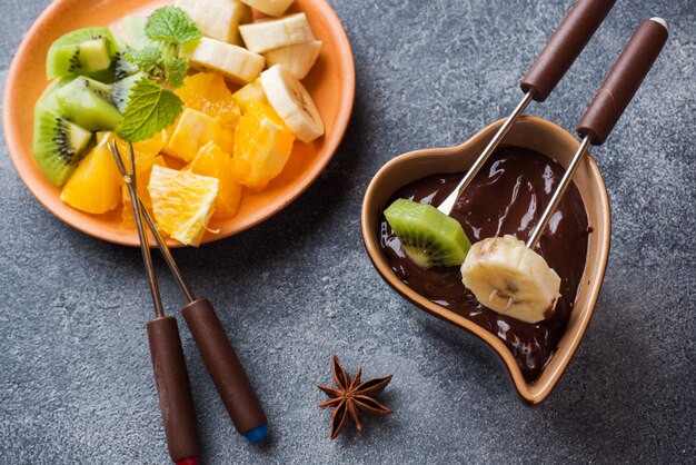 Fondue de chocolate con frutas sobre un hormigón oscuro.