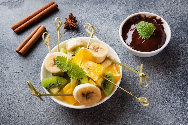 Fondue de chocolate con frutas sobre un hormigón oscuro.