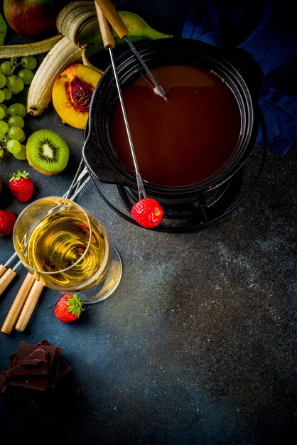Fondue de chocolate en olla de fondue tradicional, con tenedores, vino blanco, una variedad de bayas y frutas, espacio de copia