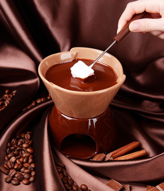 Fondue de chocolate com doces de marshmallow em fundo marrom