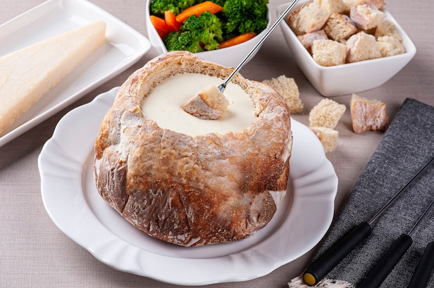 Fondue de queijo cremoso com pão italiano. Garfo mergulhando pão em cream cheese