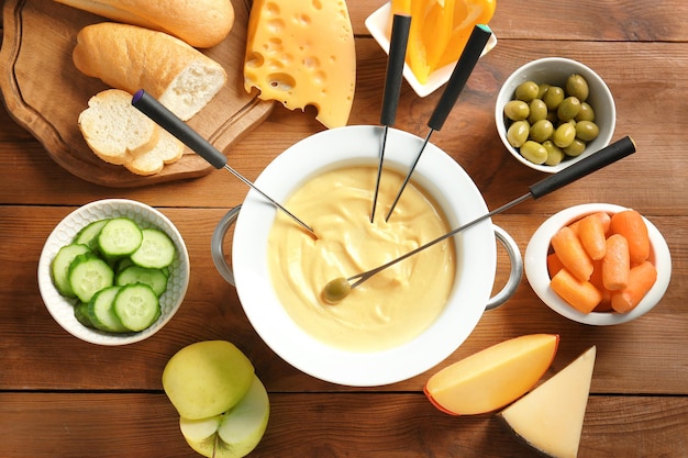 Fondue de queijo na panela e diferentes produtos na mesa de madeira