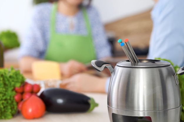 Fondue in einem Topf im Hintergrund von Freunden, die zusammen in der Nähe kochen Kücheninterieur und Kochgeschirr