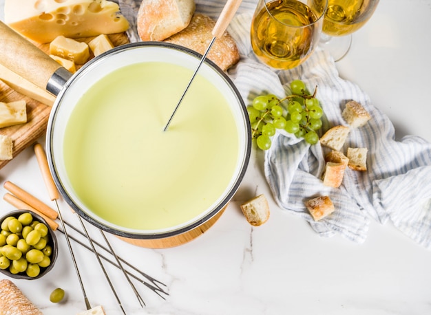 Foto fondue suíço gourmet em panela de fondue tradicional, com garfos, queijos diversos, azeitonas, pão e uva