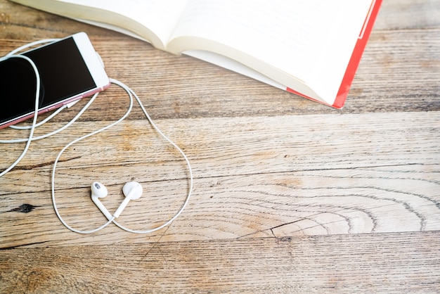 Fone de ouvido de forma de coração branco com smartphone e livro aberto na vista de topo de tabela de trabalho