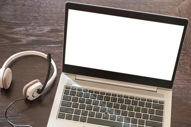 Fone de ouvido em um laptop tela branca em branco fundo de mesa de madeira