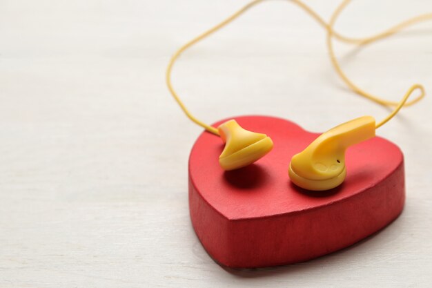 Foto fones de ouvido amarelos pequenos e coração decorativo vermelho em um fundo branco de madeira.