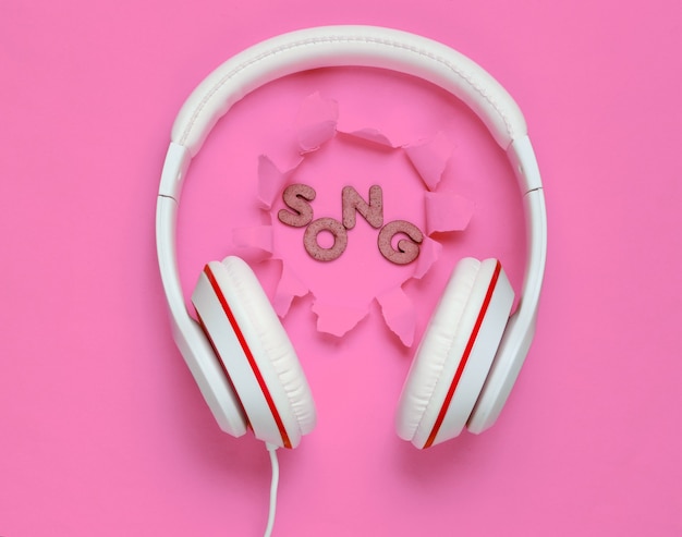Foto fones de ouvido brancos clássicos com fio em fundo de papel rosa com orifício rasgado