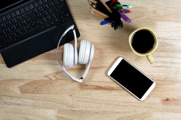 Fones de ouvido brancos e teclado na mesa de trabalho de madeira