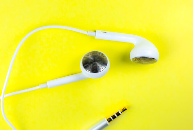 Fones de ouvido brancos sobre o fundo amarelo. Conceito de música moderna. Tecnologia de áudio. Feche a foto.