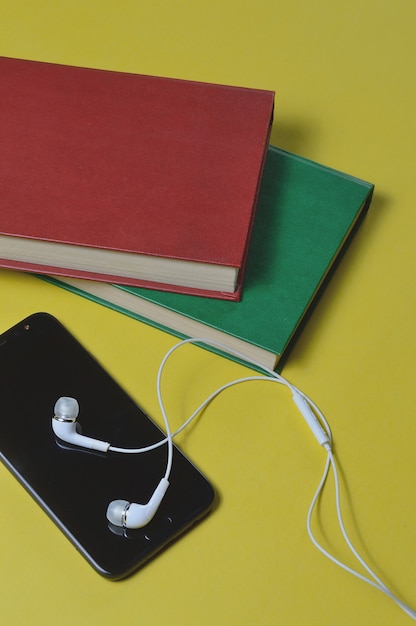 Fones de ouvido com livros e um smartphone em um fundo amarelo.