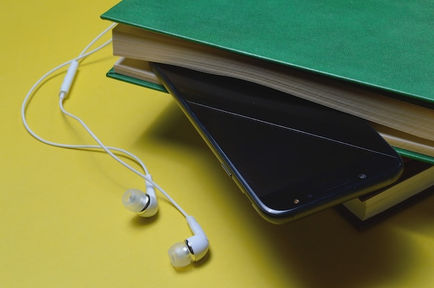 Fones de ouvido com livros e um smartphone em um fundo amarelo.