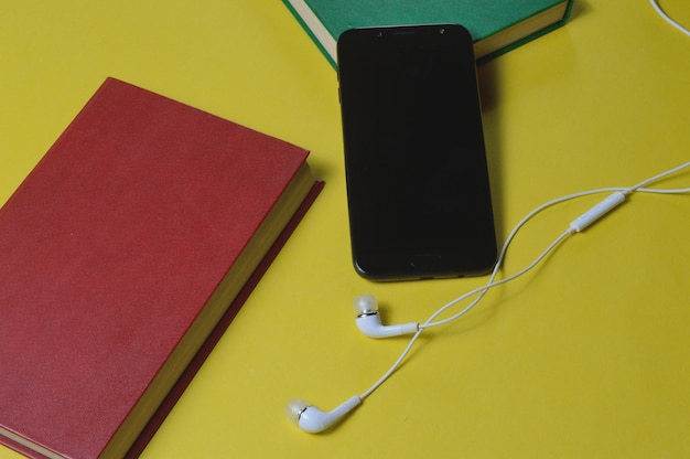 Fones de ouvido com livros e um smartphone em um fundo amarelo.