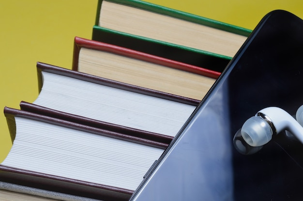 Fones de ouvido com livros e um smartphone em um fundo amarelo.