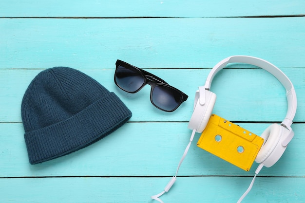 Fones de ouvido de gorro e óculos de sol com cassete de áudio em um fundo azul de madeira acessórios hipster