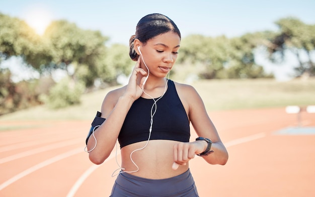 Fones de ouvido de música e verificação de pulso de mulher corredora em treinamento de treino e pausa para atletas Fitness de bem-estar e garota correndo pausa na pista do estádio para análise de desempenho no aplicativo smartwatch