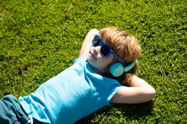 Fones de ouvido de verão frio garoto ouvindo música garoto no parque deitado na grama