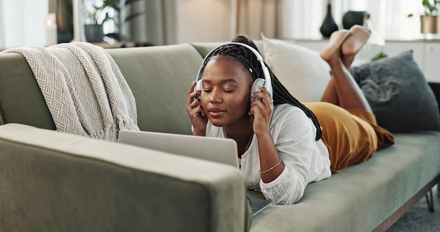fones de ouvido domésticos e mulher negra em um sofá laptop e digitação com conexão internet e streaming de música pessoa africana apartamento e garota em um sofà PC e fone de ouvido com música de som e áudio