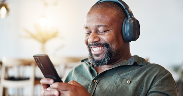 Fones de ouvido e homem preto em casa com felicidade para lista de reprodução de música on-line ou revisão de álbum Tecnologia de áudio de sorriso e homem africano com celular para streaming de podcast de rádio ou vídeo