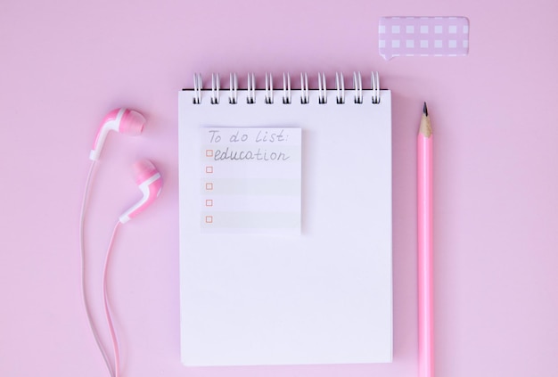 Fones de ouvido e lápis do bloco de notas em um fundo rosa