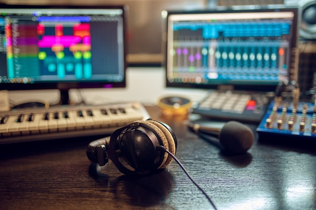 Fones de ouvido em cima da mesa, gravando o interior do estúdio no fundo. Sintetizador, mixer de áudio e monitores, local de trabalho de engenheiro de som