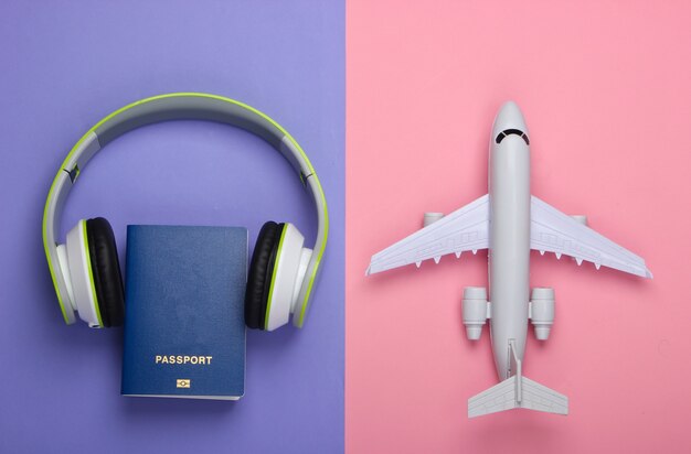 Fones de ouvido, estatueta de avião, passaporte em superfície roxa e rosa